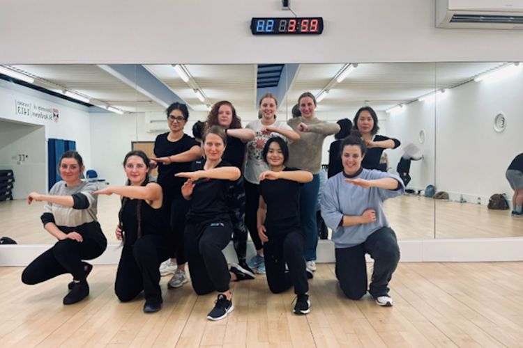 Group of women in a gym studio with their arms extended horizontally in a defensive pose