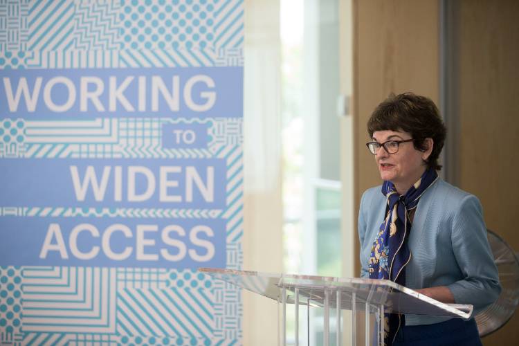 Professor Dame Sally Mapstone in front of a podium beside a projected presentation slide that reads "Working to widen access"