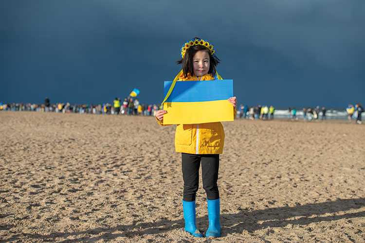 Girl in yellow jacket and blue boots standing on the beach holding a Ukraine flag