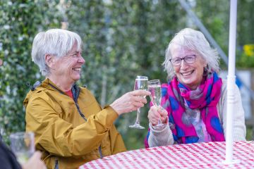 Two older ladies cheers with champagne flutes, smiling together at an informal gathering