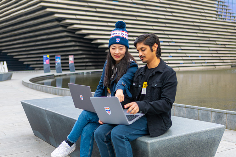 two students sitting outside with laptops