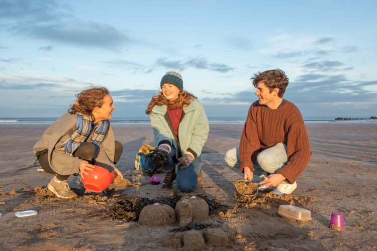 Three students sitting on the beach making sand castles