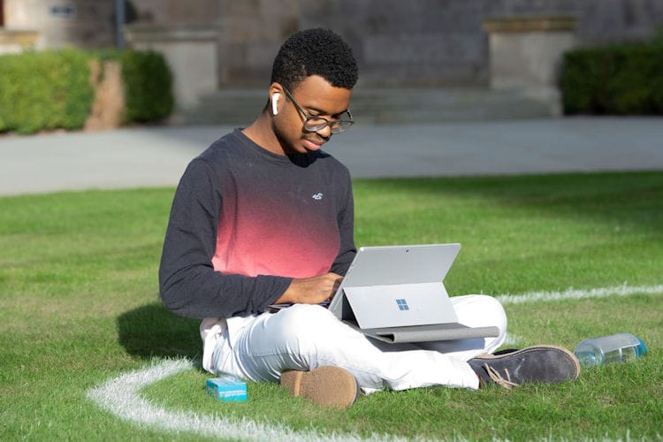 Student using a laptop while sitting on grass.