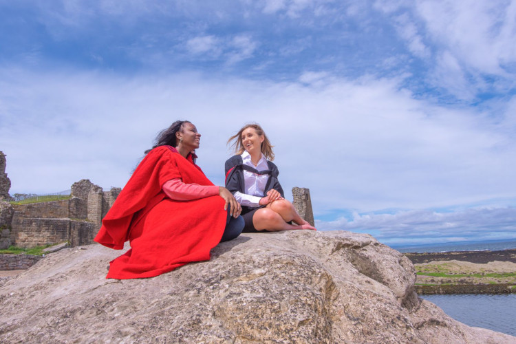 Graduate and undergraduate from the University sitting on the rocks at Castle Sands on graduation day