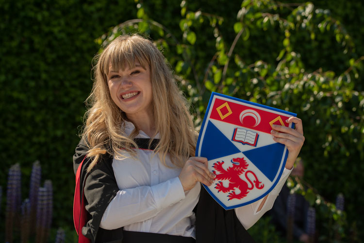 A happy graduate holding the University crest