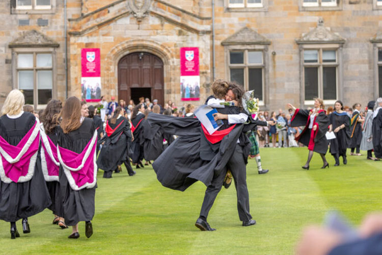 Two students embrace after graduating