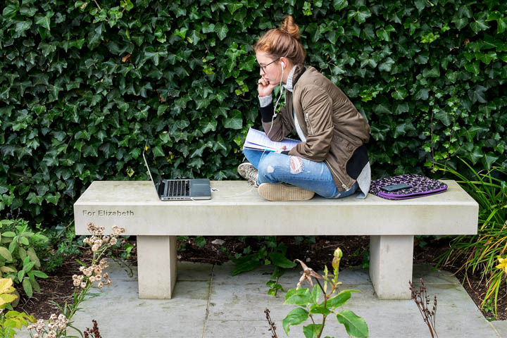 Female student sitting on a stone bench and working on her laptop