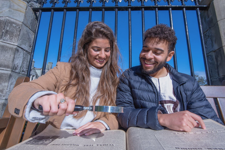 Two students looking at a publication through a magnifying glass