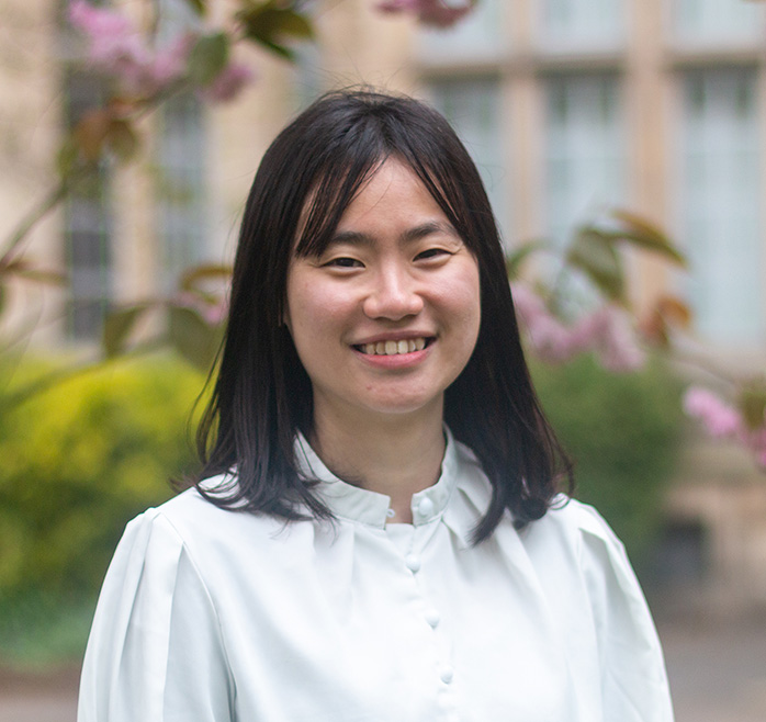 Ming Sum Kong, dressed in a white shirt, stood in from of a cherry blossom tree.