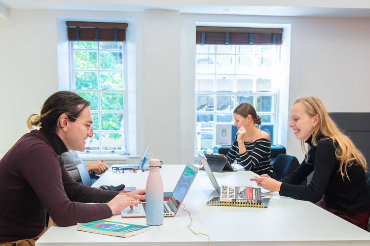 Students sit around a table working with laptop computers and books
