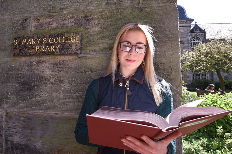 Student with a book, stood outside of St Mary's College Library
