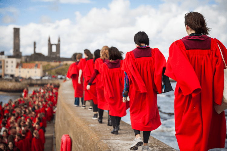 Student in red gowns walk down the St Andrews pier