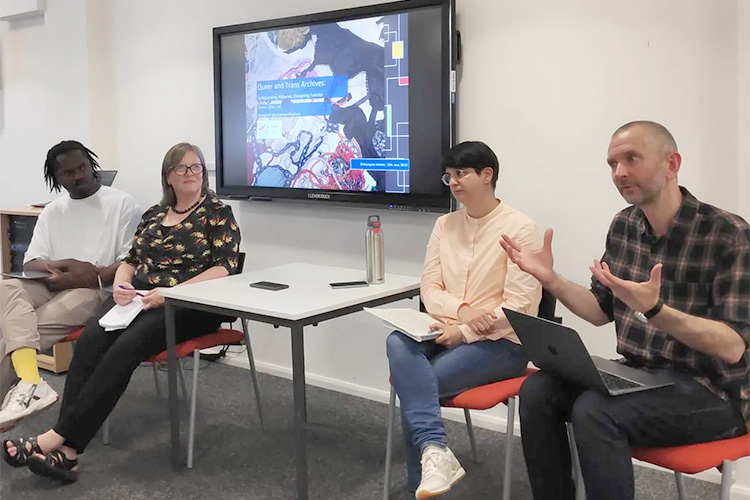 A man is speaking alongside three other people seated in front of a screen