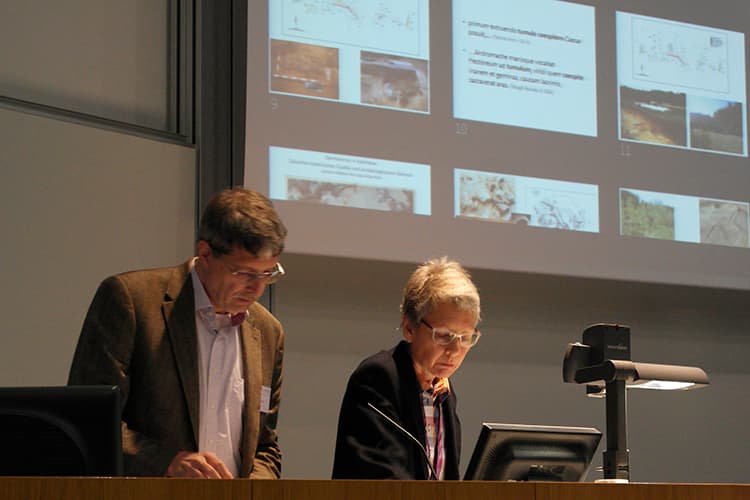 two people standing at a podium with a powerpoint presentation on the screen behind them