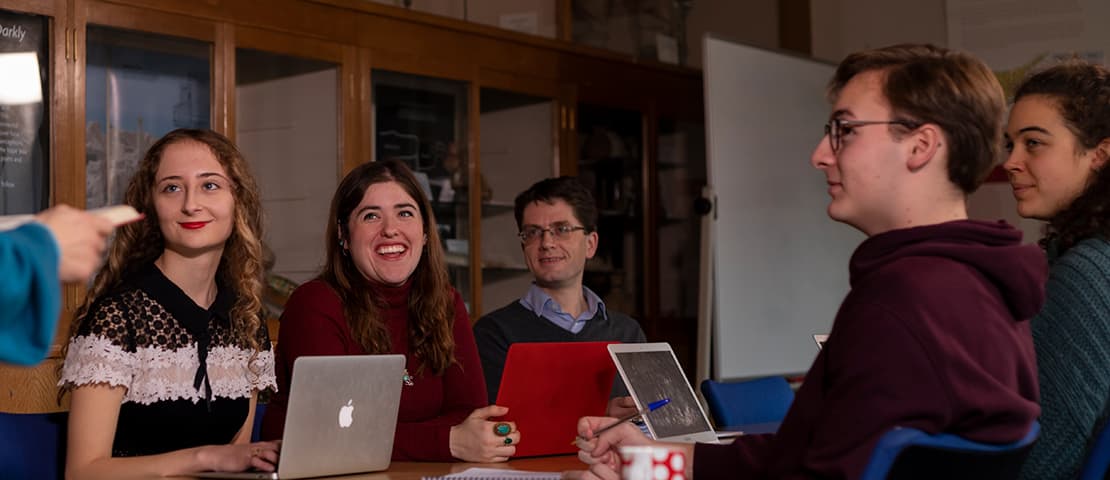 people sitting round a table with laptops smiling at speaker who is off-camera