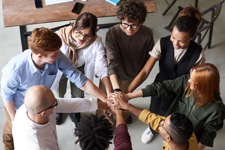 People standing in a circle with hands joined in the centre of the group.