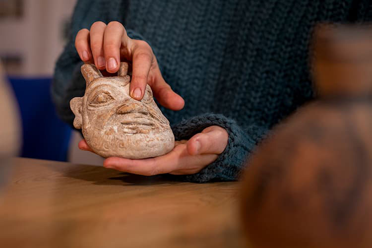 person in blue jumper holding a small stone sculpture of a satyr's face.