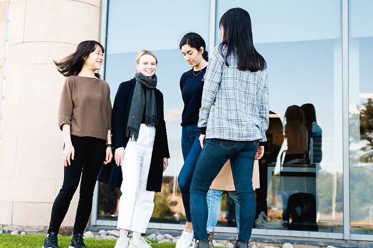 four students standing outside the Gateway, with reflections in the windows