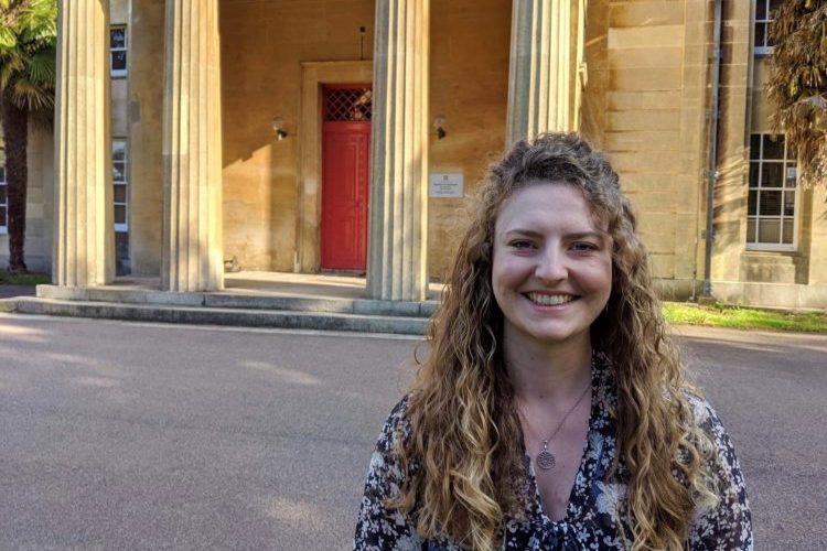 Amy, a female student, standing in front of a building in the summer.