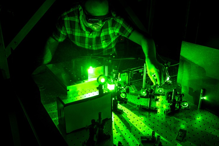 PhD student is adjusting laser equipment on an optical bench.