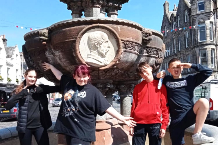Group of First Chances Fife students from second year of secondary smiling in front of Whyte-Melville Memorial Fountain in St Andrews