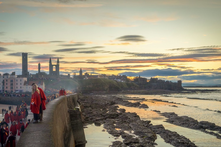 Students in red gown stand on St Andrews pier in the sunset