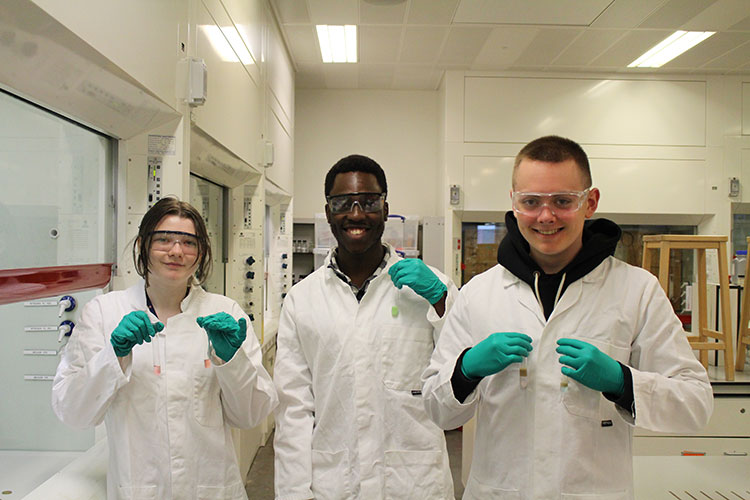Three students in lab coats holding up test tubes