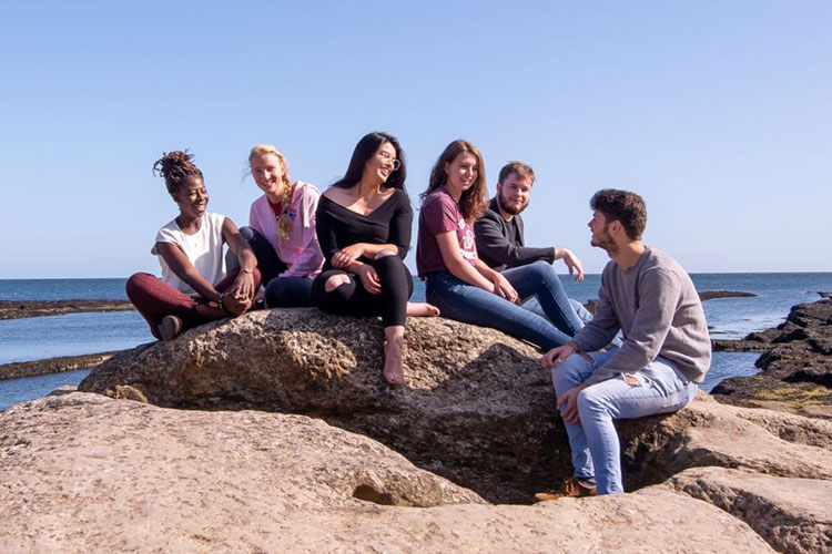 Students sitting on a rock by the beach