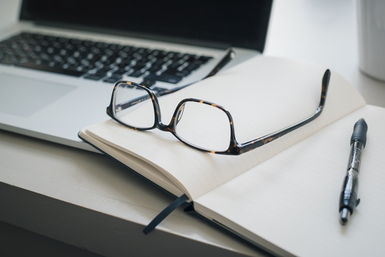 Pari of spectacles laid on a notebook next to a laptop