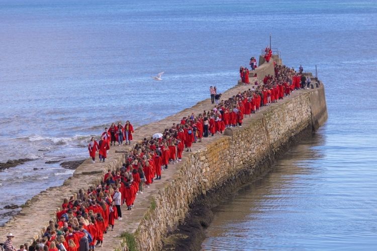 A large group of students dressed in red academic gowns walking along St Andrews Pier